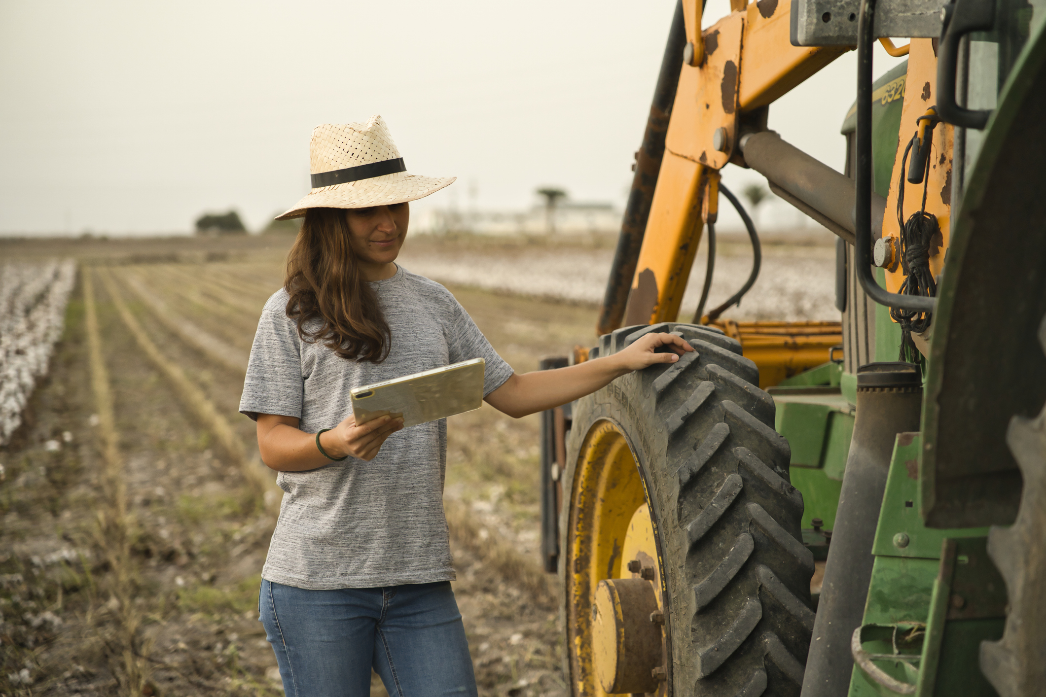 Portrait of smiling young woman farmer using tablet and tractor for harvest. Modern agriculture with the concept of technology and machinery Portrait of smiling young woman farmer using tablet and tractor for harvest. Modern agriculture with the concept of technology and machinery